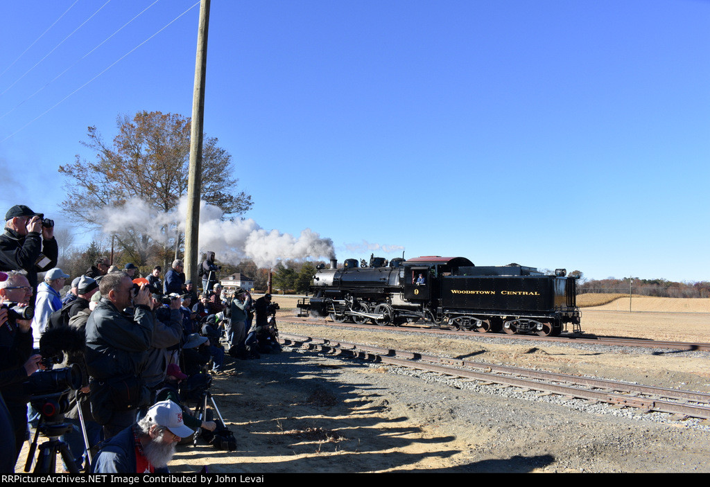 The proud group of photographers in the photo line video and photograph the 0-6-0 9 steam locomotive making a reverse move on the main track toward the freight cars. 